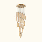 A modern multi-light linear chandelier with a brushed gold circular canopy and multiple hanging clear glass cylinder shades of varying lengths, shown against a plain off-white background.
