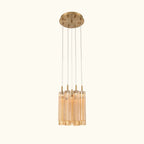 A modern multi-light linear pendant chandelier with a brushed gold ceiling canopy, suspension rods, and clear glass cylindrical shades that glow warm white when lit, shown against a plain white background.
