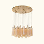 A modern multi-light chandelier with a brushed gold circular canopy, multiple thin suspension rods, and clear cylindrical glass shades, shown against a plain white background.