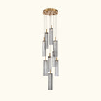 A modern multi-light linear chandelier with six clear ribbed glass cylinders suspended from a round brushed gold ceiling canopy by thin metal rods.