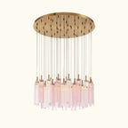 A modern multi-light chandelier pendant fixture with a circular brushed brass canopy, clear glass rods, and multiple pink-tinted glass cylinder drops, shown against a solid white background.