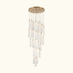 A modern multi-light chandelier with a brushed gold circular canopy and multiple clear cylindrical glass shades of varying lengths, suspended against a plain white background.