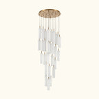 A modern multi-light linear chandelier with a brushed gold circular canopy and multiple clear cylindrical glass shades of varying lengths, suspended against a plain white background.