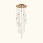 A modern multi-light chandelier with a circular brushed gold ceiling canopy, multiple hanging clear glass cylindrical shades of varying lengths, and warm white light emission, shown against a plain white background.