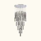 A modern multi-light chandelier with a circular silver canopy and multiple tiers of hanging cylindrical glass shades in brushed silver and smoked gray, shown against a plain white background.