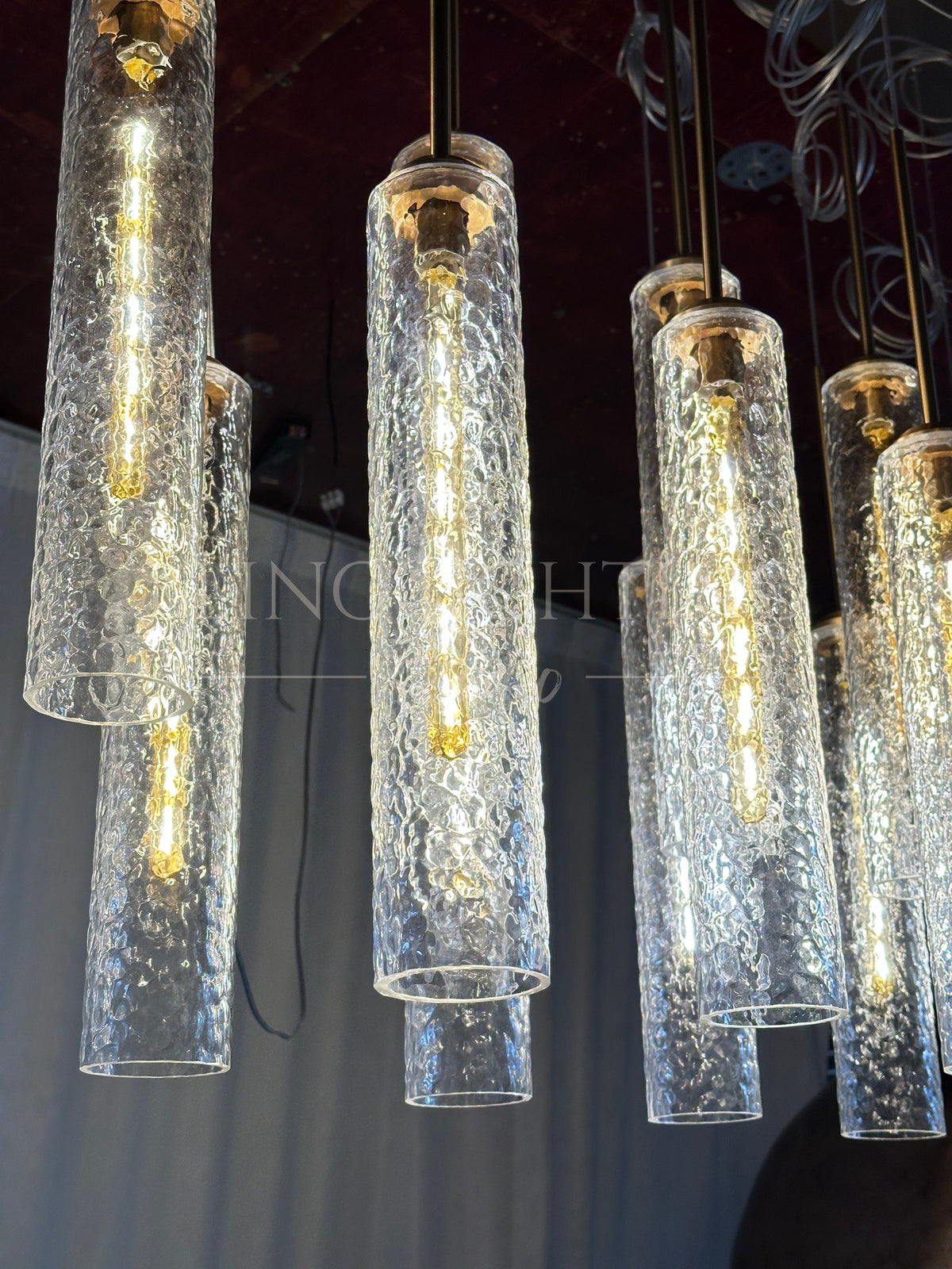 Colleena linear chandelier showing illuminated hammered glass cylinders at staggered heights