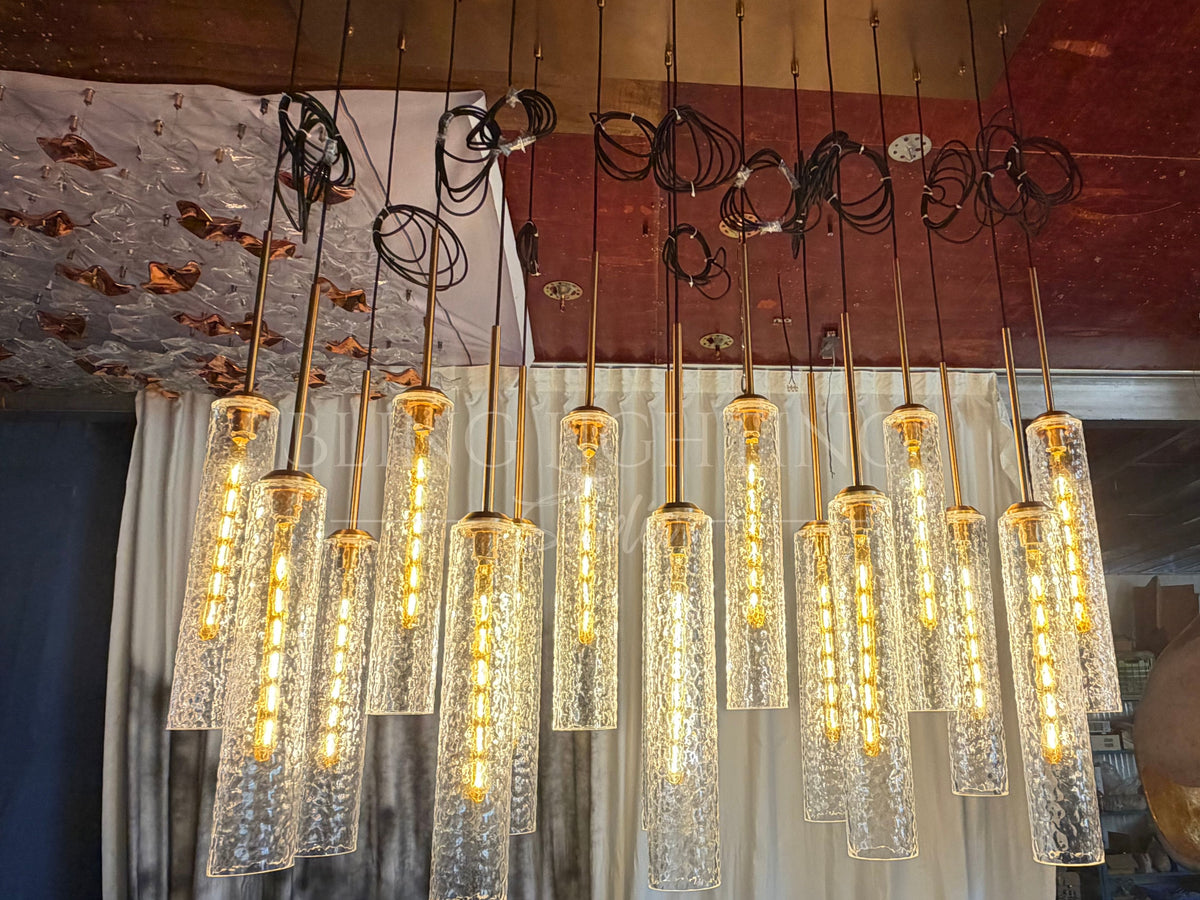 Front view of the Colleena hammered glass chandelier with clear cylinder shades in a wide linear arrangement