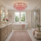 A luxurious spa-style bathroom featuring a large pink glass chandelier, a freestanding white bathtub with a pink towel, a matching pink patterned rug, and a light wood vanity with gold fixtures.