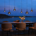 Cleo Bubble smoke glass pendant chandelier above a lakeside dining table at dusk