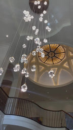 Modern Crystal Chandelier for High Ceiling Living Room beside a staircase with glass railing and gold accents