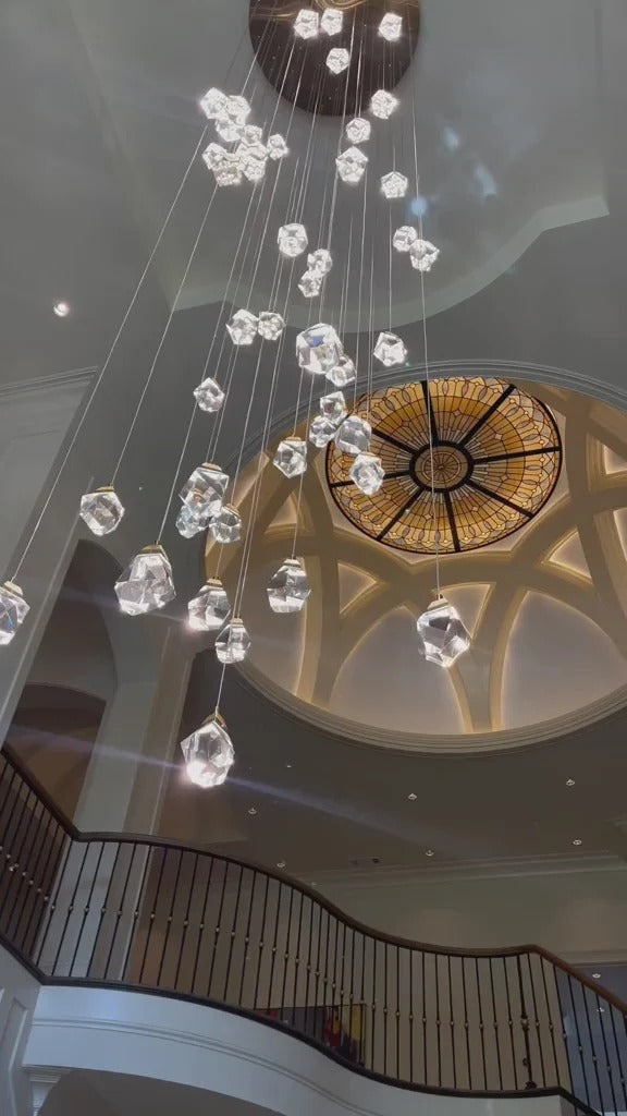 Modern Crystal Chandelier for High Ceiling Living Room beside a staircase with glass railing and gold accents