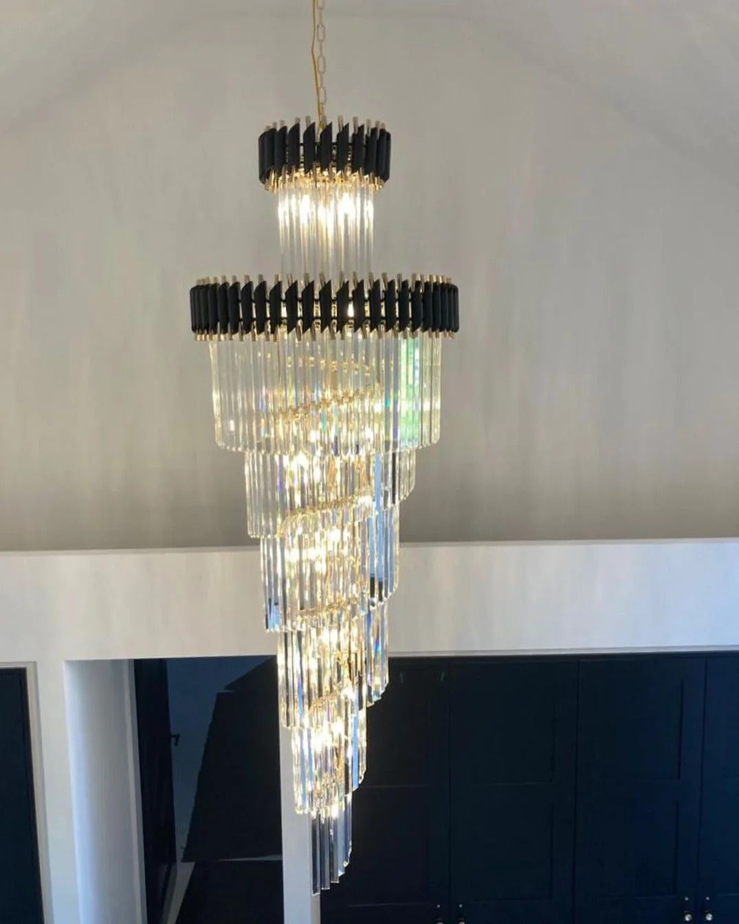 Olivia Crystal Modern Stair Chandelier installed against a high wall with layered crystal tiers