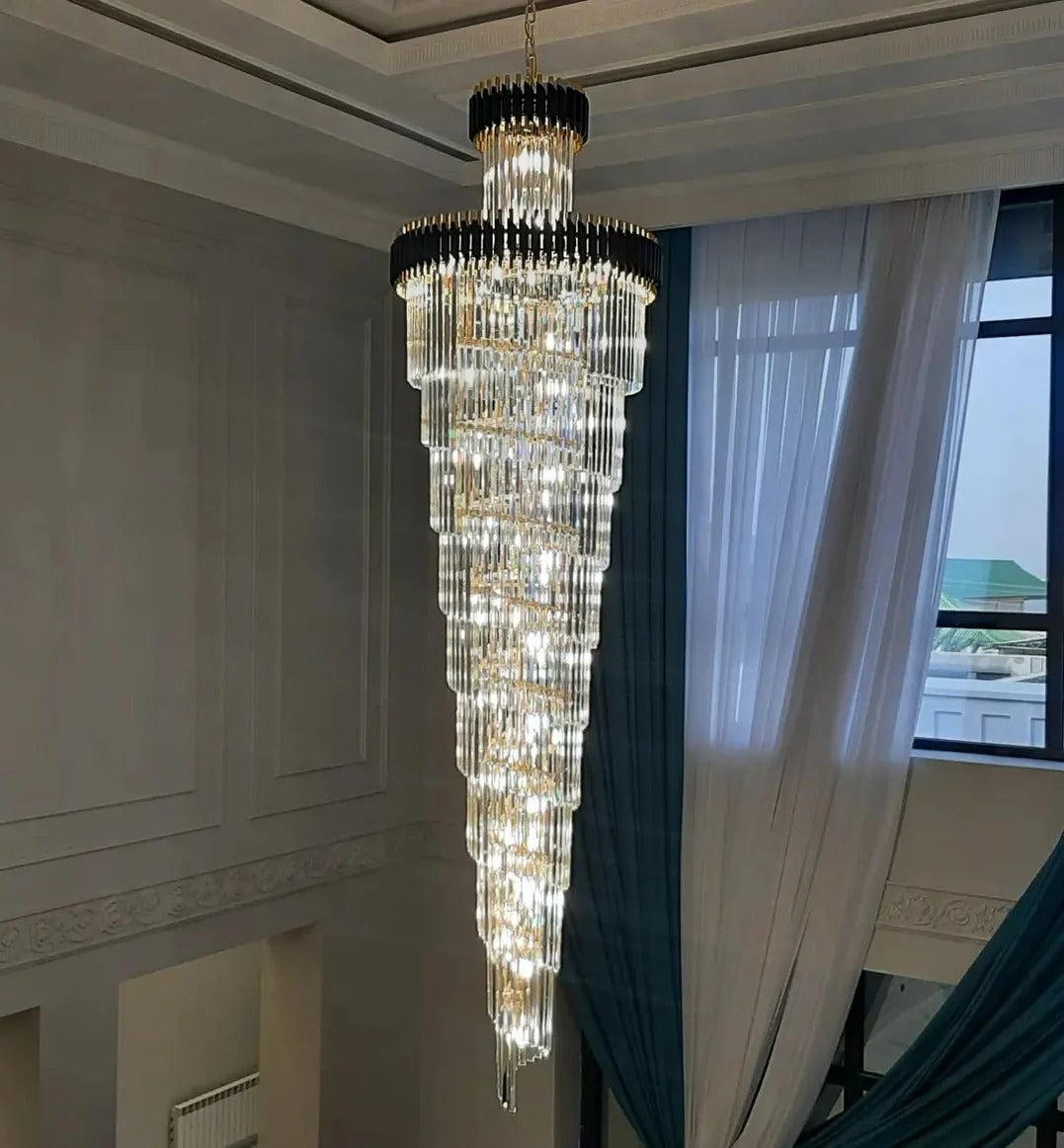 Olivia Crystal Modern Stair Chandelier installed in a high ceiling space beside tall windows and curtains