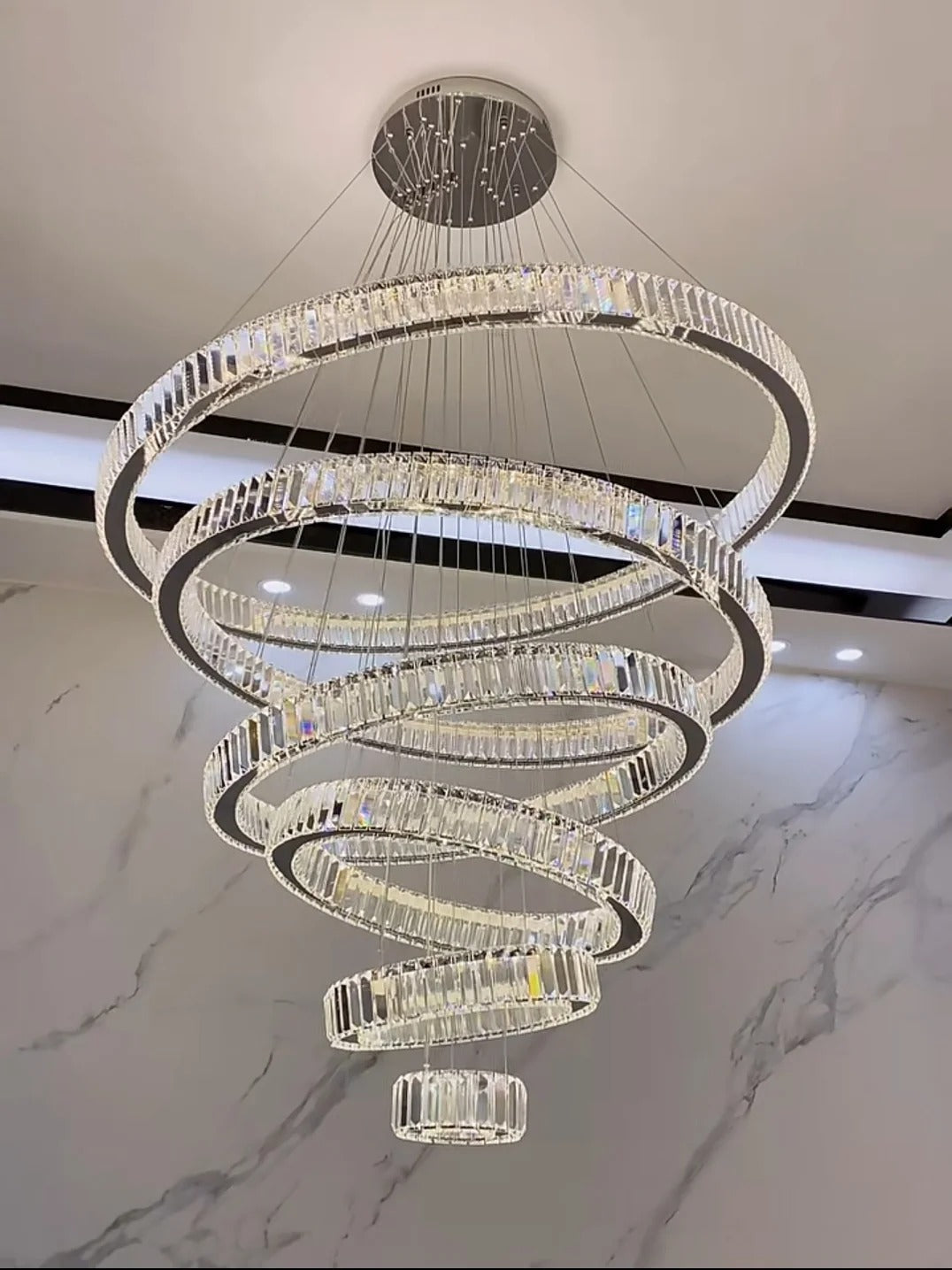 6 Tier Crystal Ring Chandelier for High Ceiling chrome finish installed near a marble wall